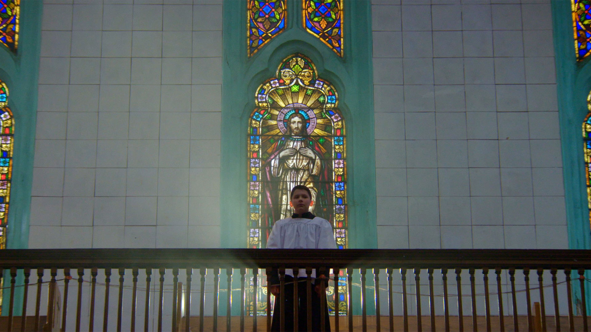 Trailer still frame from Procession, young boy standing in front of Jesus glass mosaic